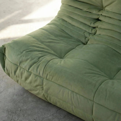 Close up of a corner of the the Bruma 3 seater sofa in Green Velvet Suede by vibehaus on a concrete floor.