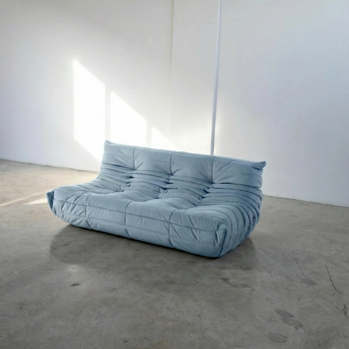 Bruma 3 seater sofa in light blue Velvet Suede by vibehaus on a concrete floor, photographed from a side angle.
