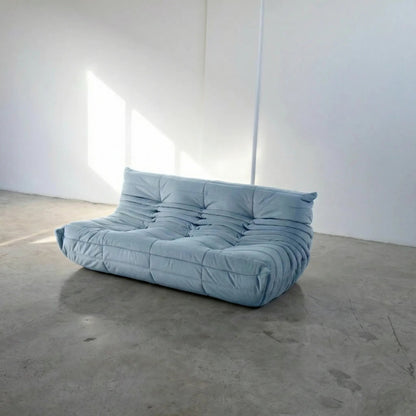 Bruma 3 seater sofa in light blue Velvet Suede by vibehaus on a concrete floor, photographed from a side angle.