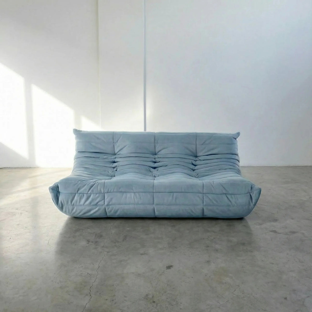 Bruma 3 seater sofa in light blue Velvet Suede by vibehaus on a concrete floor, photographed from a front angle.