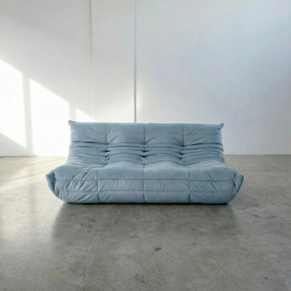 Bruma 3 seater sofa in light blue Velvet Suede by vibehaus on a concrete floor, photographed from a front angle.