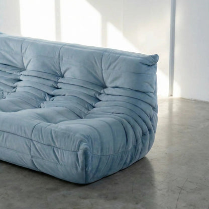 Close up of the corner of the Bruma 3 seater sofa in light blue Velvet Suede by vibehaus on a concrete floor, photographed from a side angle.