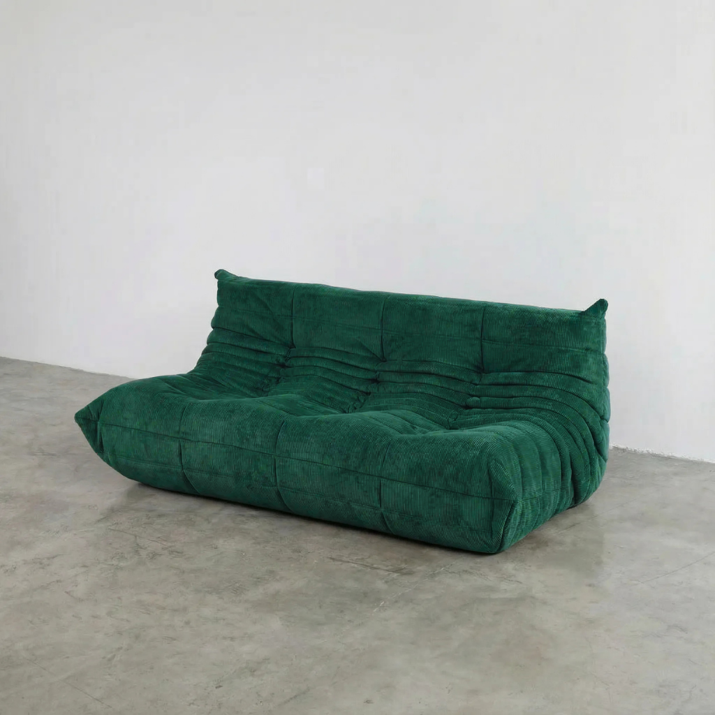 Bruma 3 seater sofa in dark green Corduroy by vibehaus on a concrete floor, photographed from a side angle.