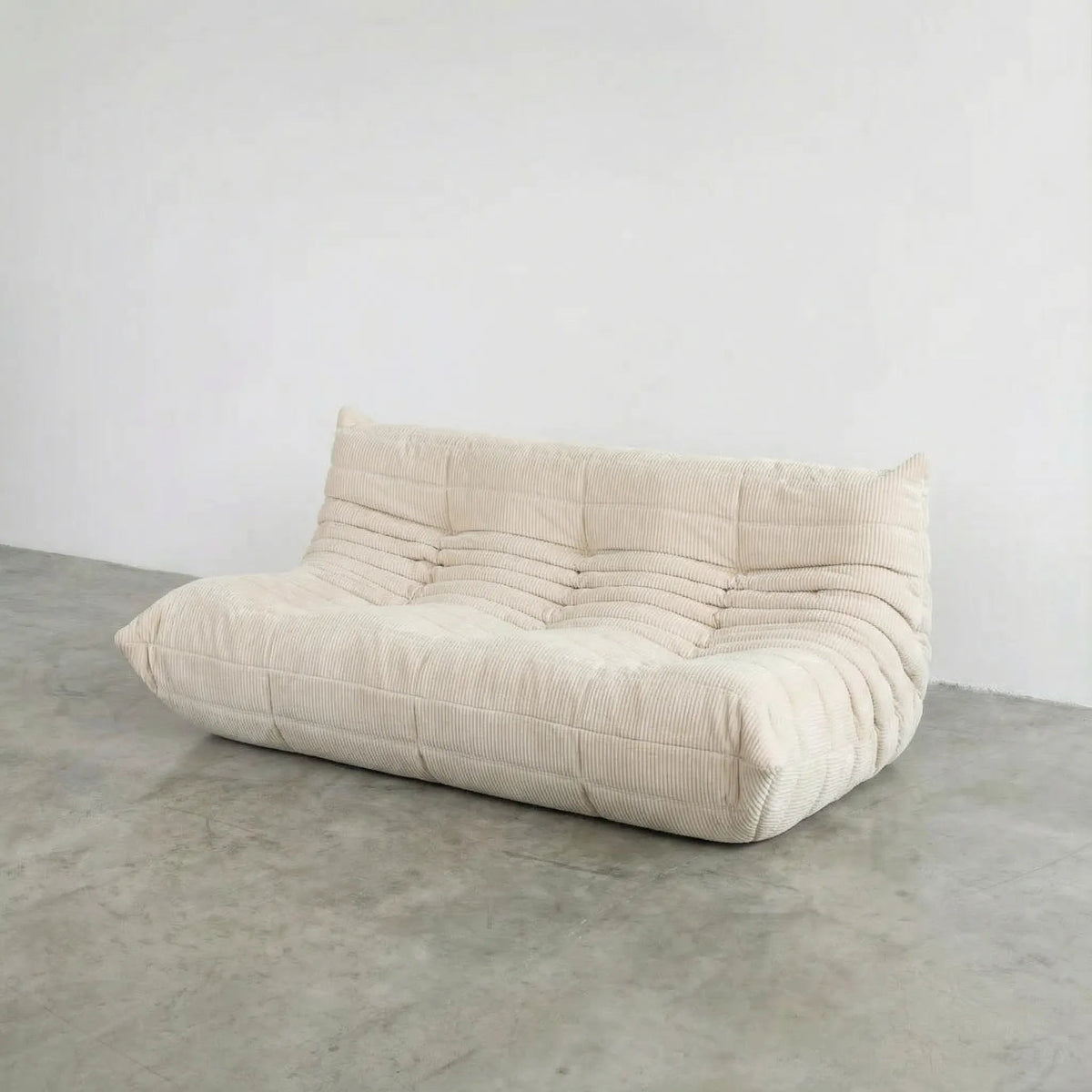 Bruma 3 seater sofa in cream Corduroy by vibehaus on a concrete floor, photographed from a side angle.