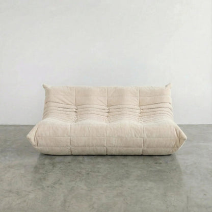 Bruma 3 seater sofa in cream Corduroy by vibehaus on a concrete floor, photographed from a front angle.