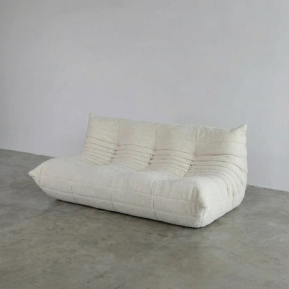 Bruma 3 seater sofa in white bouclé by vibehaus on a concrete floor, photographed from a side angle.