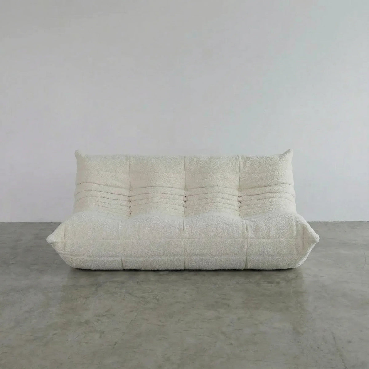 Bruma 3 seater sofa in white bouclé by vibehaus on a concrete floor, photographed from a front angle.