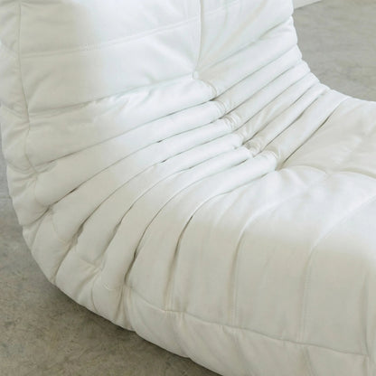 Close up of the Bruma Chair in white faux leather on a concrete floor with a white wall background