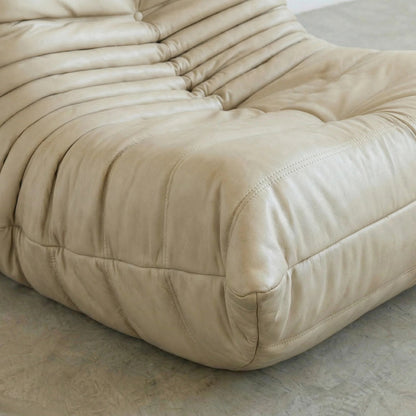 close-up of the Bruma Chair in cream real cowhide leather on a concrete floor with a white wall background