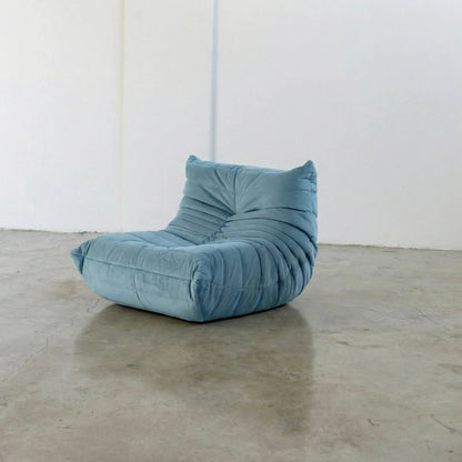 Handmade Bruma sofa chair in light blue velvet suede on a concrete floor with a white wall background