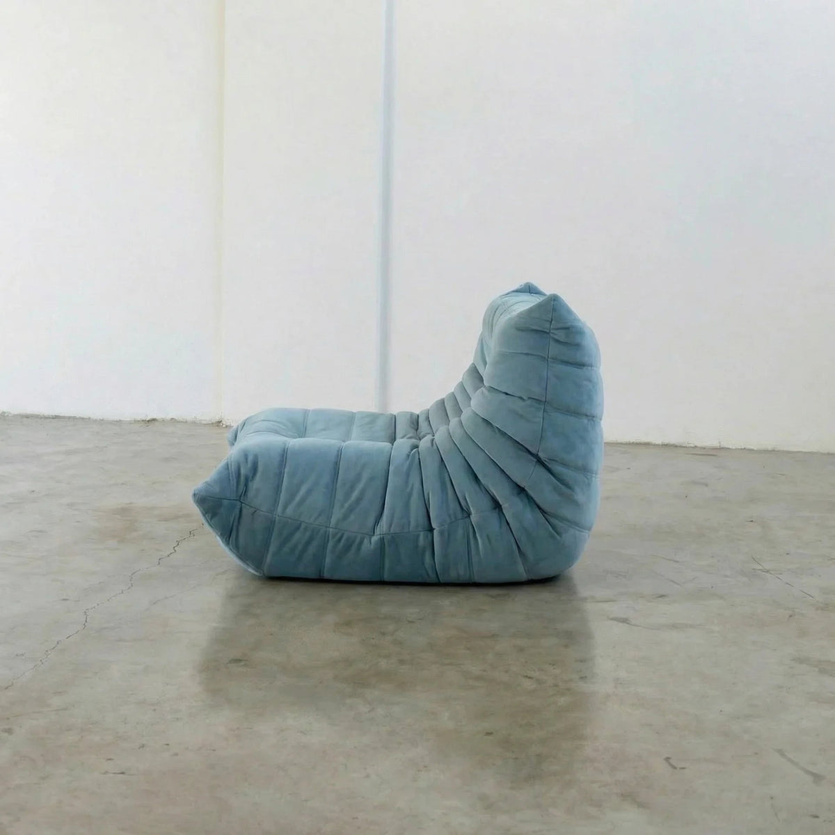 Handmade Bruma sofa chair in light blue velvet suede on a concrete floor with a white wall background