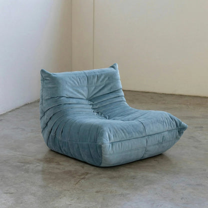 Handmade Bruma sofa chair in light blue velvet suede on a concrete floor with a white wall background