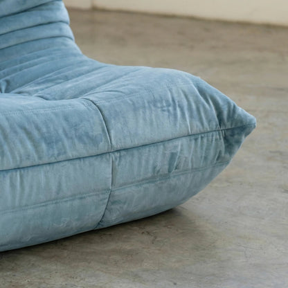 Close up of the handmade Bruma sofa chair in light blue velvet suede on a concrete floor with a white wall background