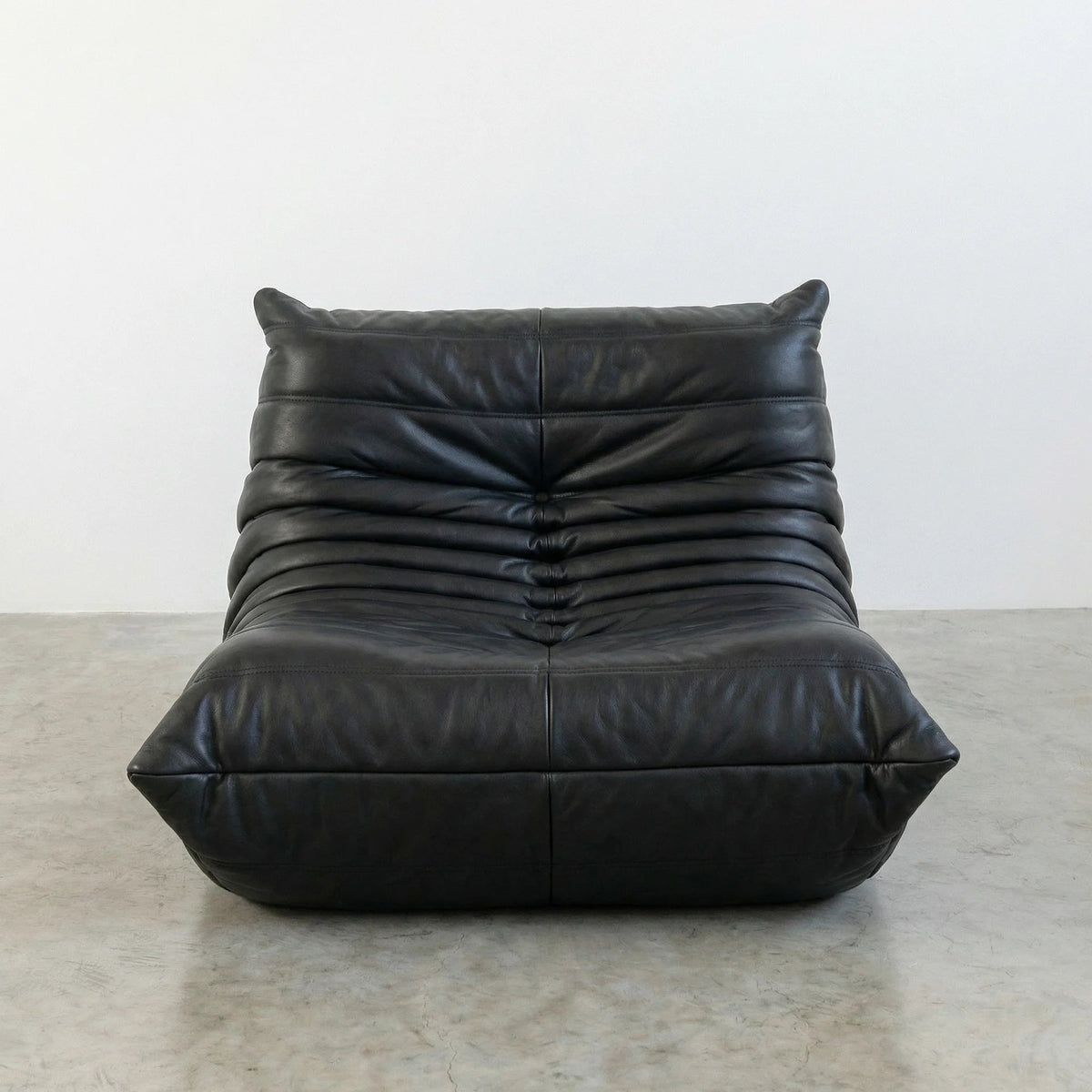 Bruma Chair in black real cowhide leather on a concrete floor with a white wall background