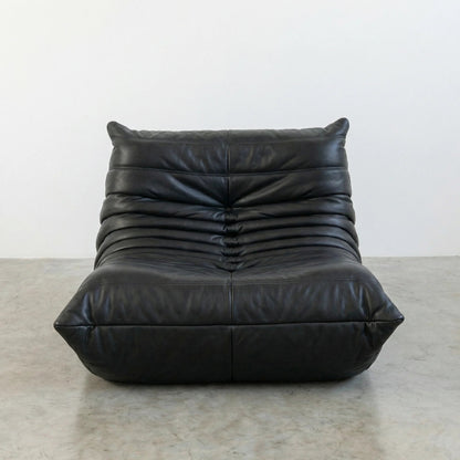 Bruma Chair in black real cowhide leather on a concrete floor with a white wall background