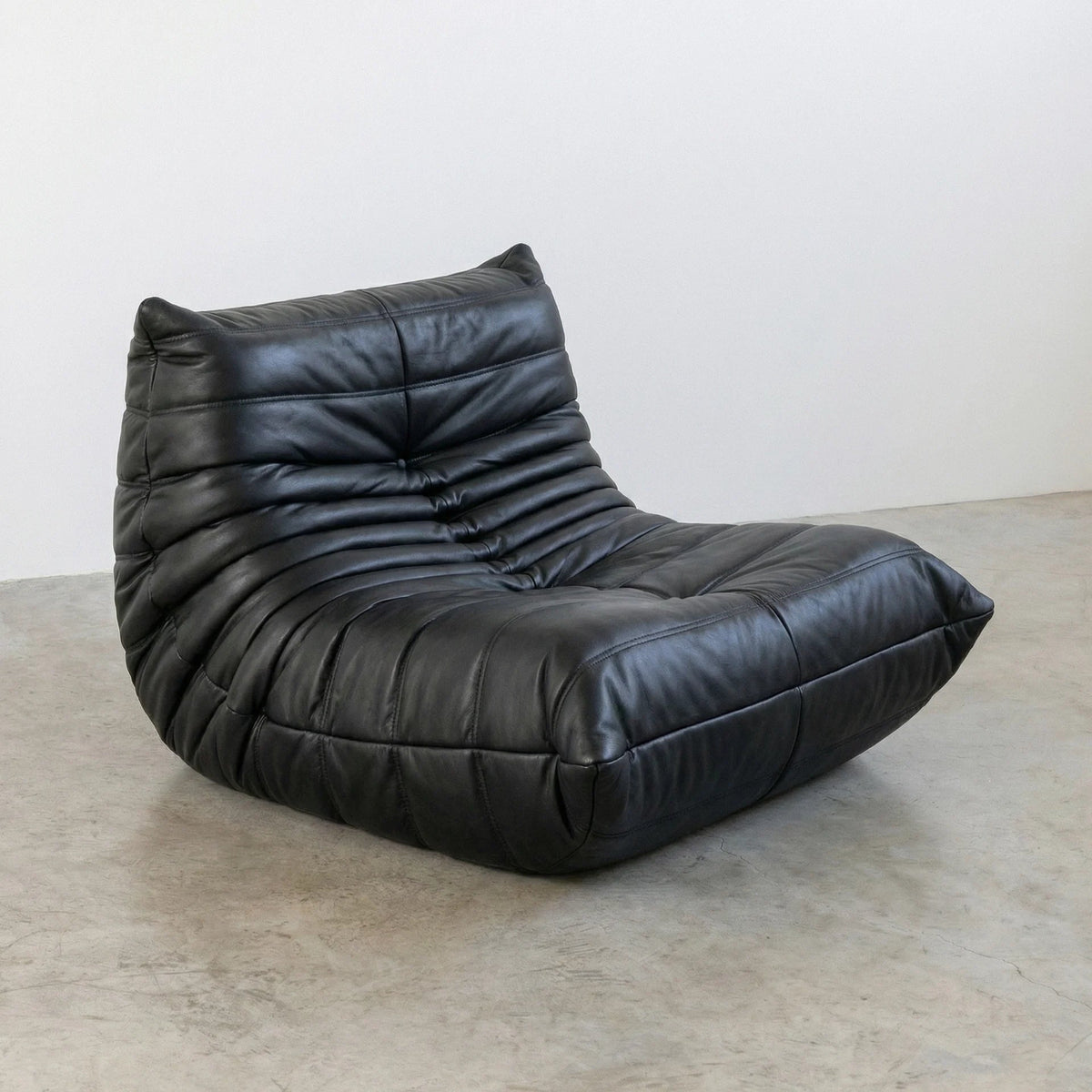Bruma Chair in black real cowhide leather on a concrete floor with a white wall background