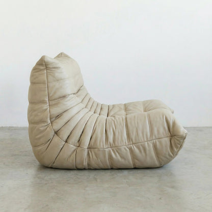Bruma Chair in cream real cowhide leather on a concrete floor with a white wall background, shot from a side angle