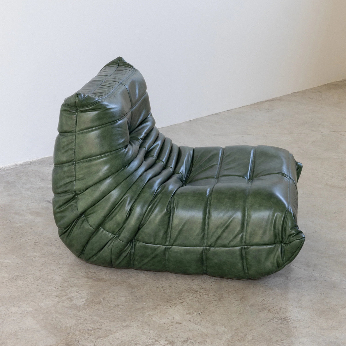 Bruma Chair in green real shiny oil wax leather on a concrete floor with a white wall background