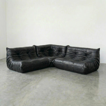 Black leather sectional Bruma sofa on a concrete floor with a white wall background