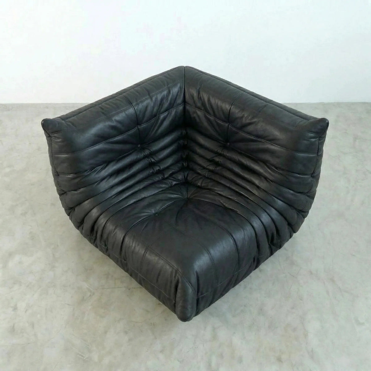 Bruma Corner Section in black real leather on a concrete floor with a white wall background