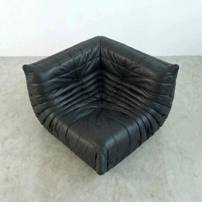 Bruma Corner Section in black real leather on a concrete floor with a white wall background