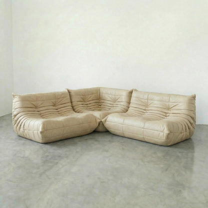 Cream Beige leather Bruma sectional sofa on a concrete floor with a white wall background