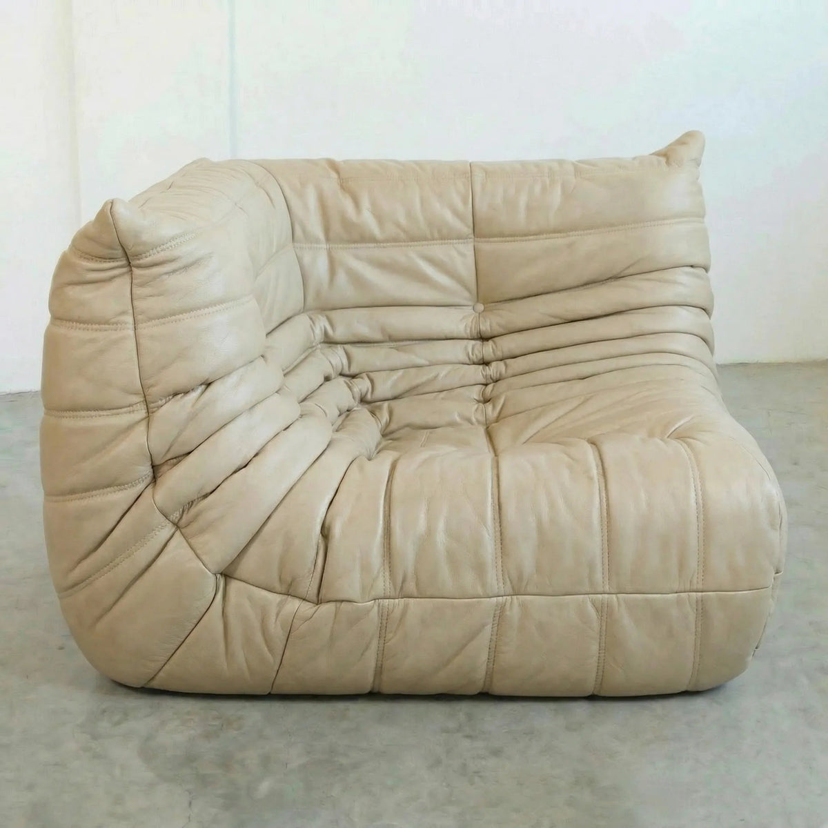 Bruma Corner Section in beige leather on a concrete floor with a white wall background