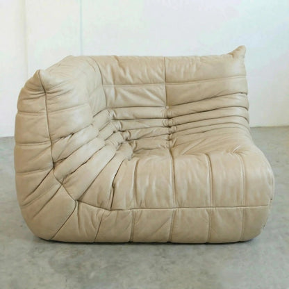 Bruma Corner Section in beige leather on a concrete floor with a white wall background