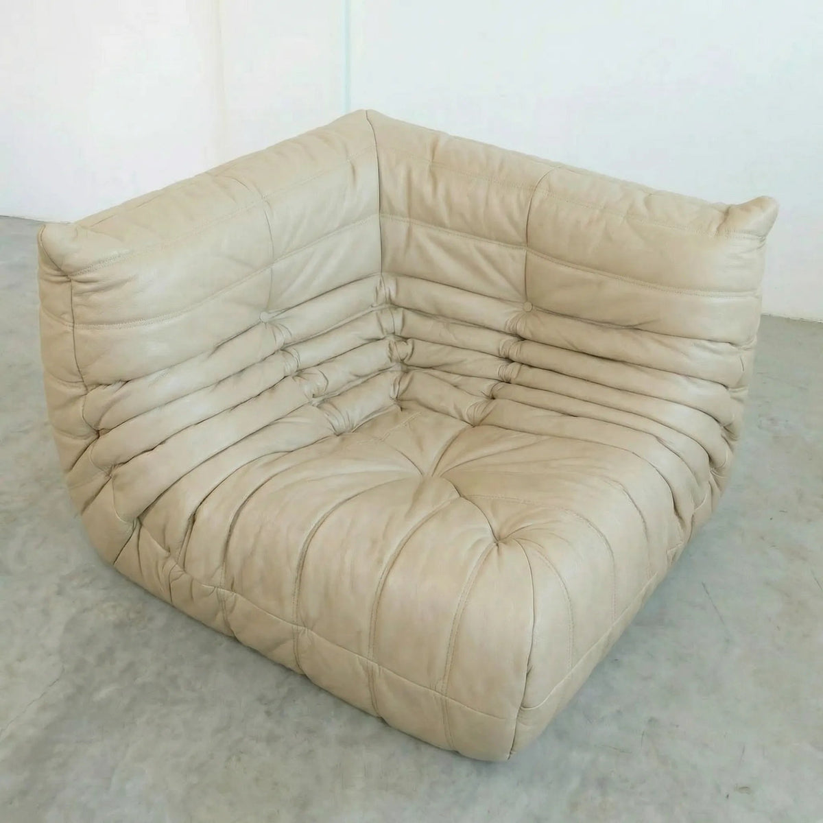 Bruma Corner Section in beige leather on a concrete floor with a white wall background
