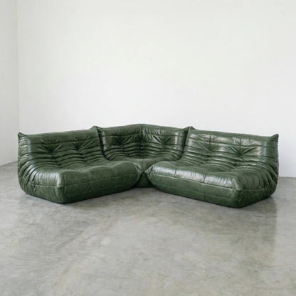 Green leather Bruma sectional sofa set on a concrete floor with a white wall background