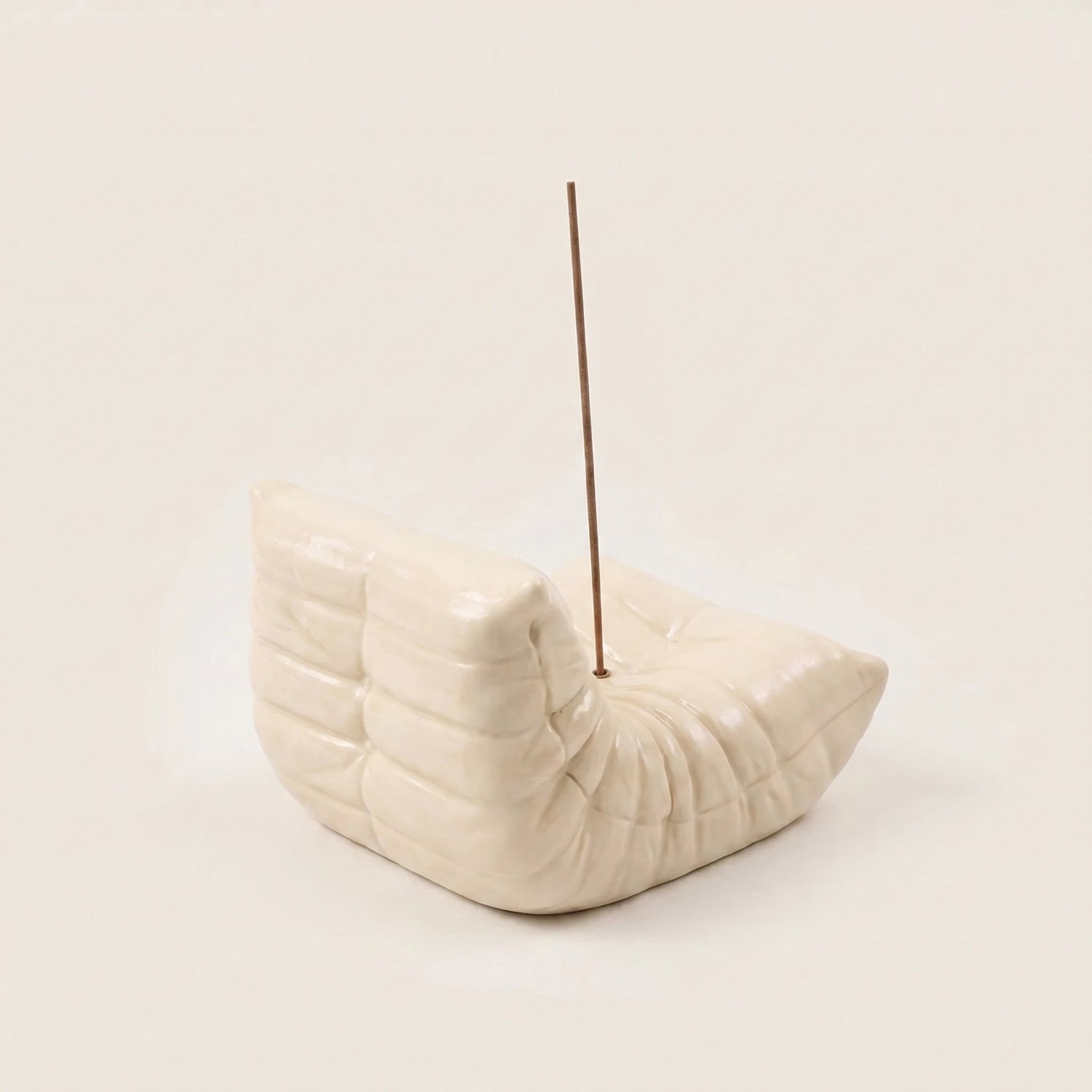 Cream Bruma incense holder shaped like a mini pleated lounge chair with an incense stick on a beige background.