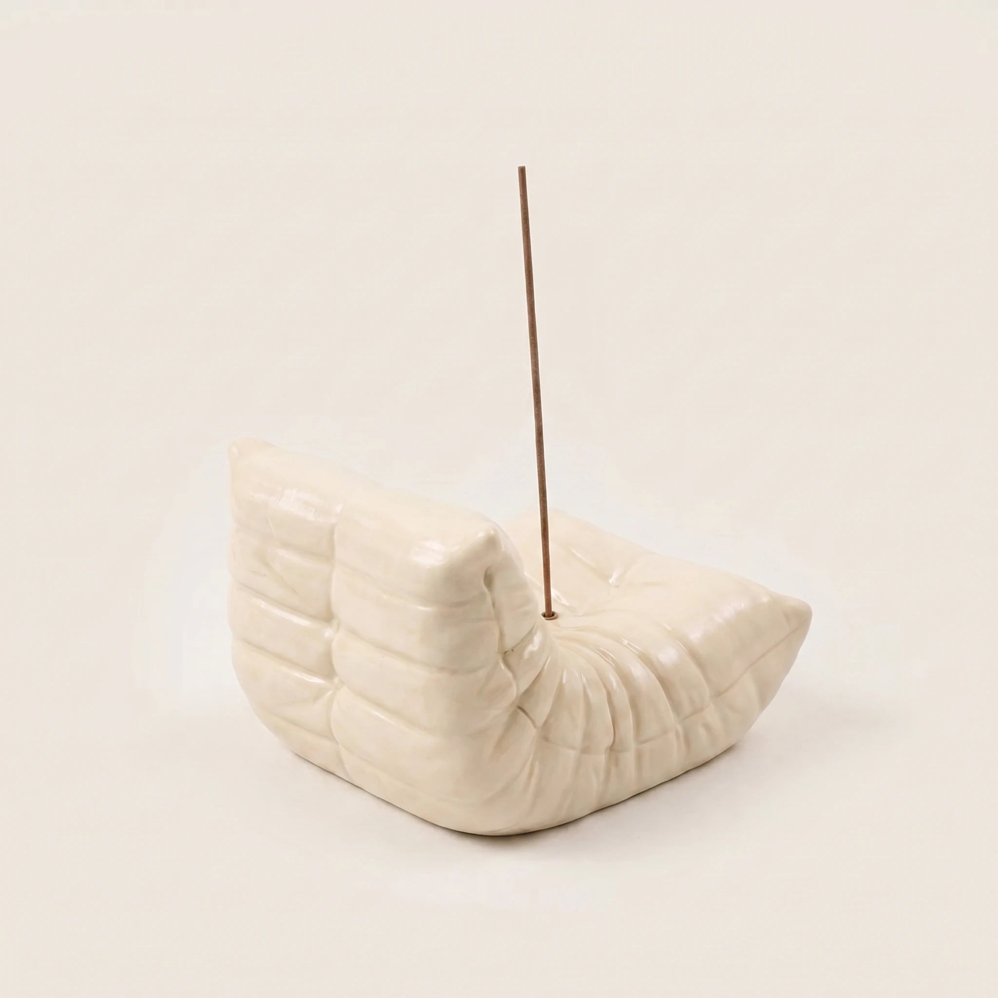 Cream Bruma incense holder shaped like a mini pleated lounge chair with an incense stick on a beige background.