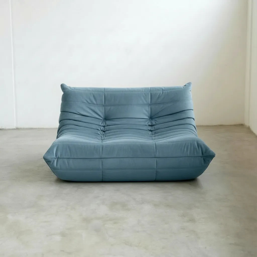 Light Blue Bruma Sofa in Velvet Suede on a concrete floor with a white wall background, photographed from the front