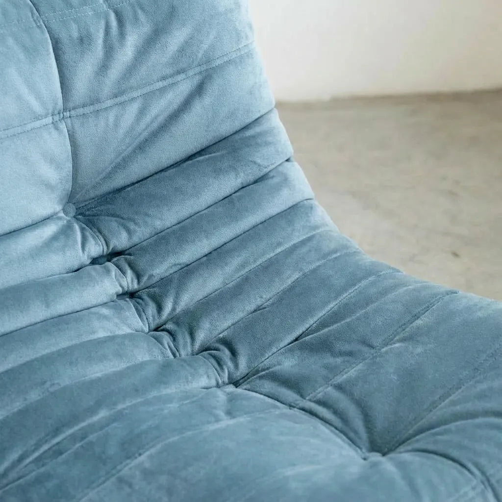 Close-up of a Light Blue Bruma Sofa in Velvet Suede on a concrete floor with a white wall background