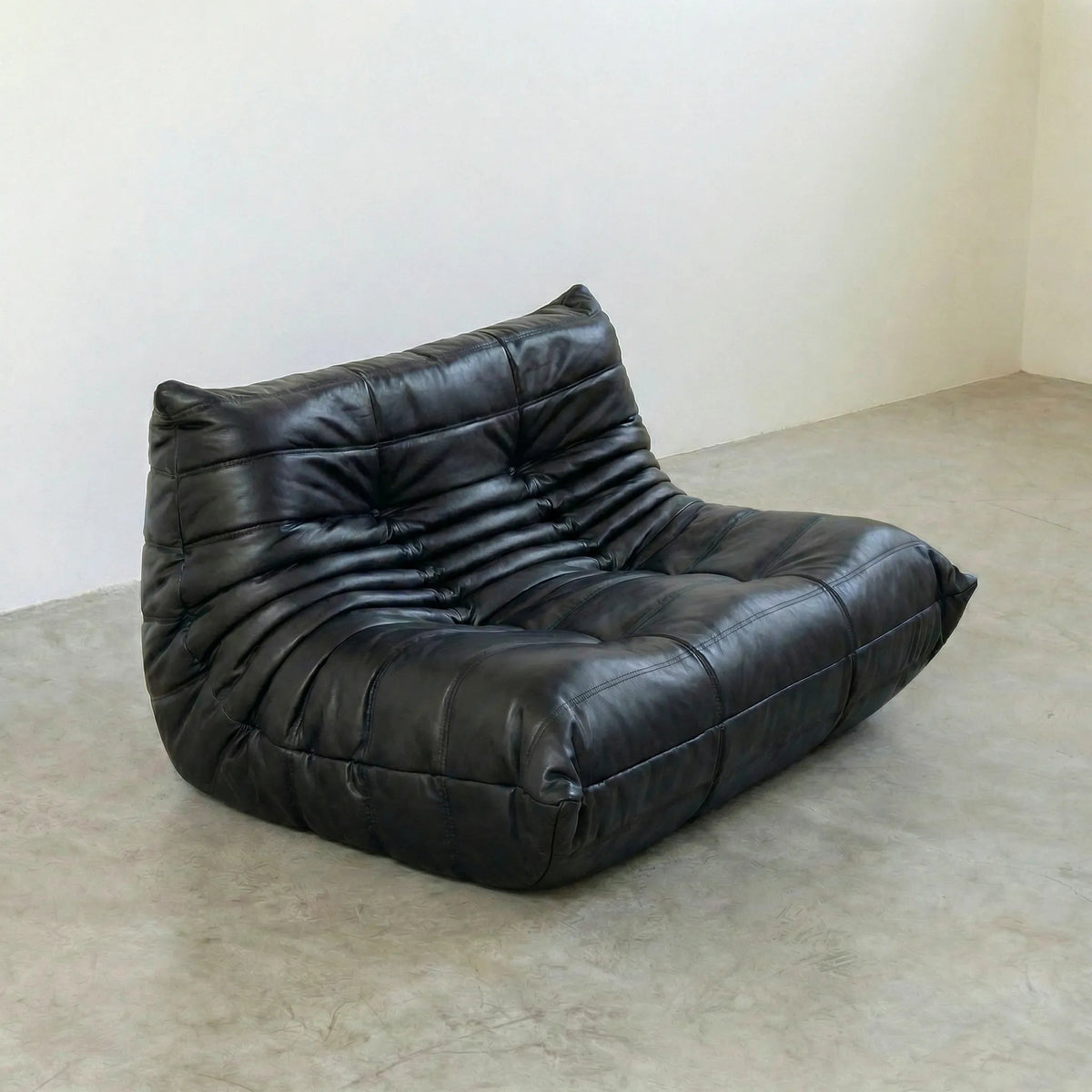 Bruma sofa in black leather on a concrete floor with a white wall background