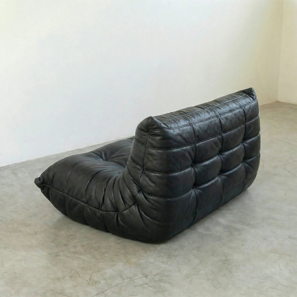 Bruma sofa in black leather on a concrete floor with a white wall background