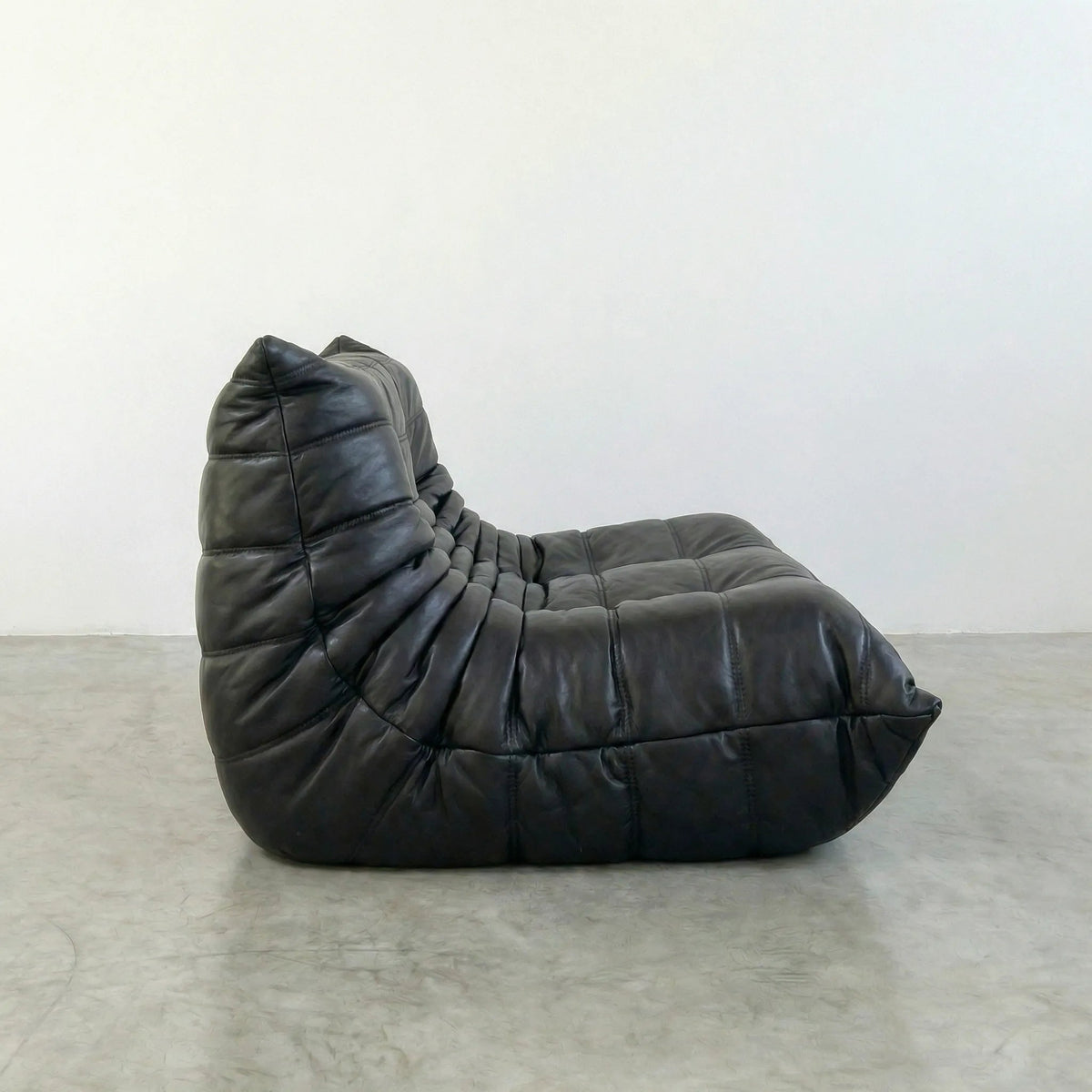 Bruma sofa in black leather on a concrete floor with a white wall background