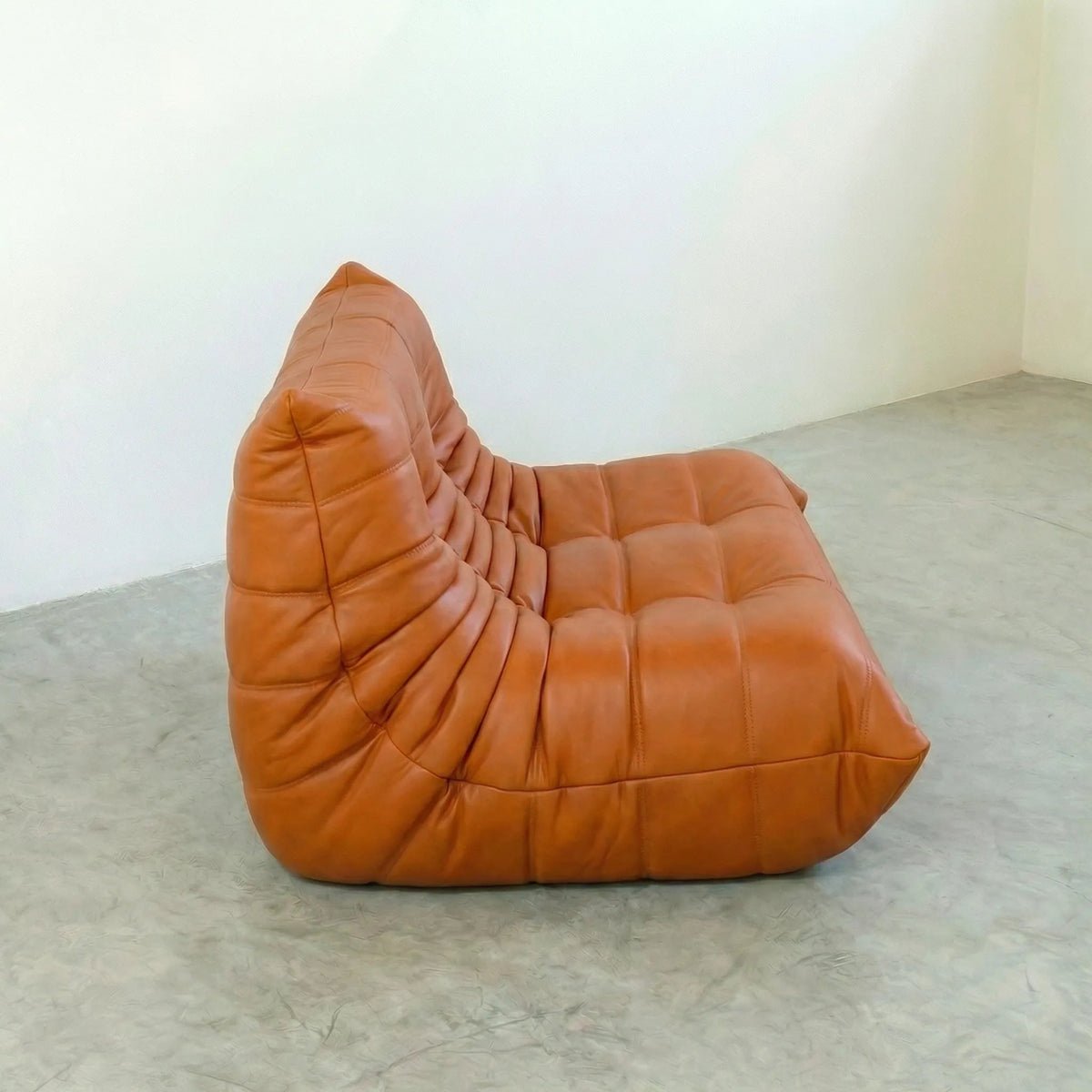 Orange leather Bruma sofa on a concrete floor with a white wall background