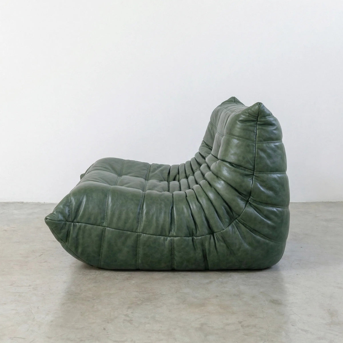 Green Bruma sofa in leather on a concrete floor with a white wall background