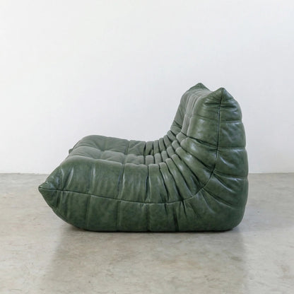 Green Bruma sofa in leather on a concrete floor with a white wall background