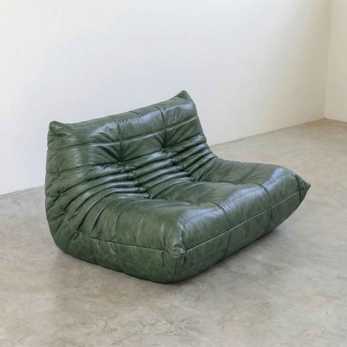 Green Bruma sofa in leather on a concrete floor with a white wall background
