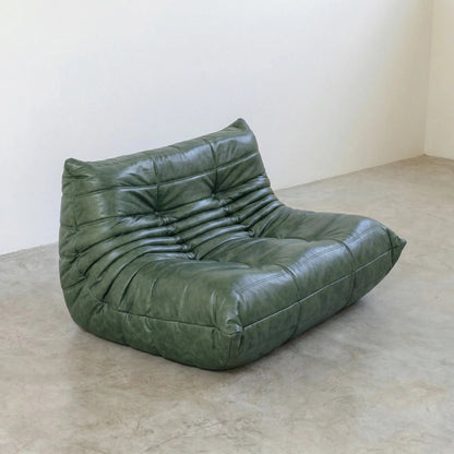 Green Bruma sofa in leather on a concrete floor with a white wall background