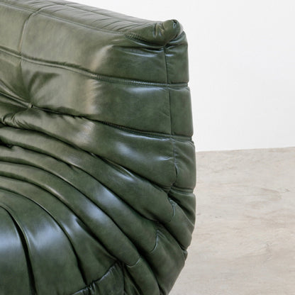 Close-up of the Bruma Chair in green real shiny oil wax leather on a concrete floor with a white wall background