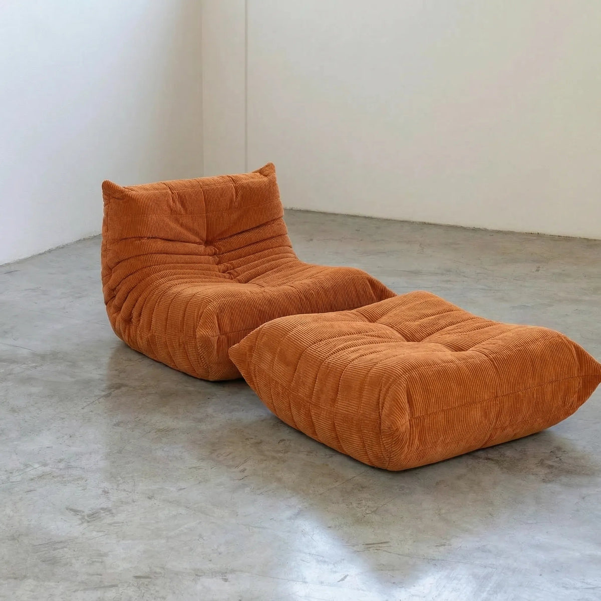 Orange corduroy Bruma chair and ottoman by Vibehaus on a concrete floor