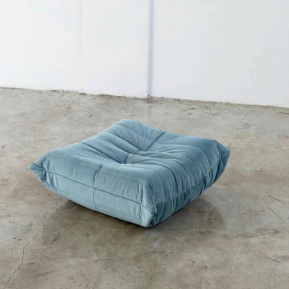 Blue Bruma-styled ottoman in velvet suede by vibehaus on a concrete floor with white walls
