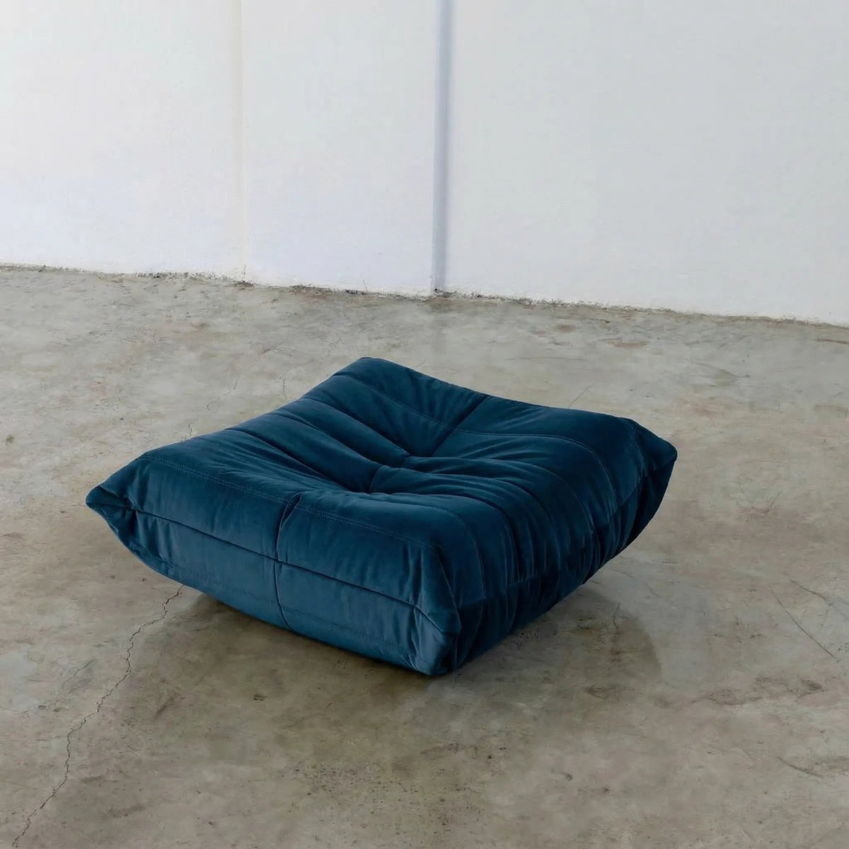 Dark Blue Bruma-styled ottoman in velvet suede by vibehaus on a concrete floor with white walls