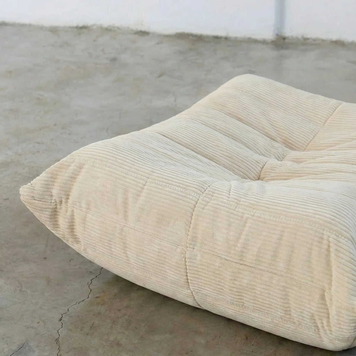 Close-up of cream Bruma ottoman in corduroy on a concrete floor