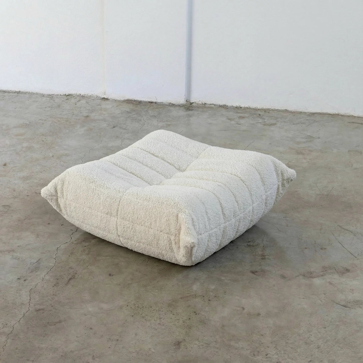 White Bruma-styled ottoman in bouclé by vibehaus on a concrete floor with white walls