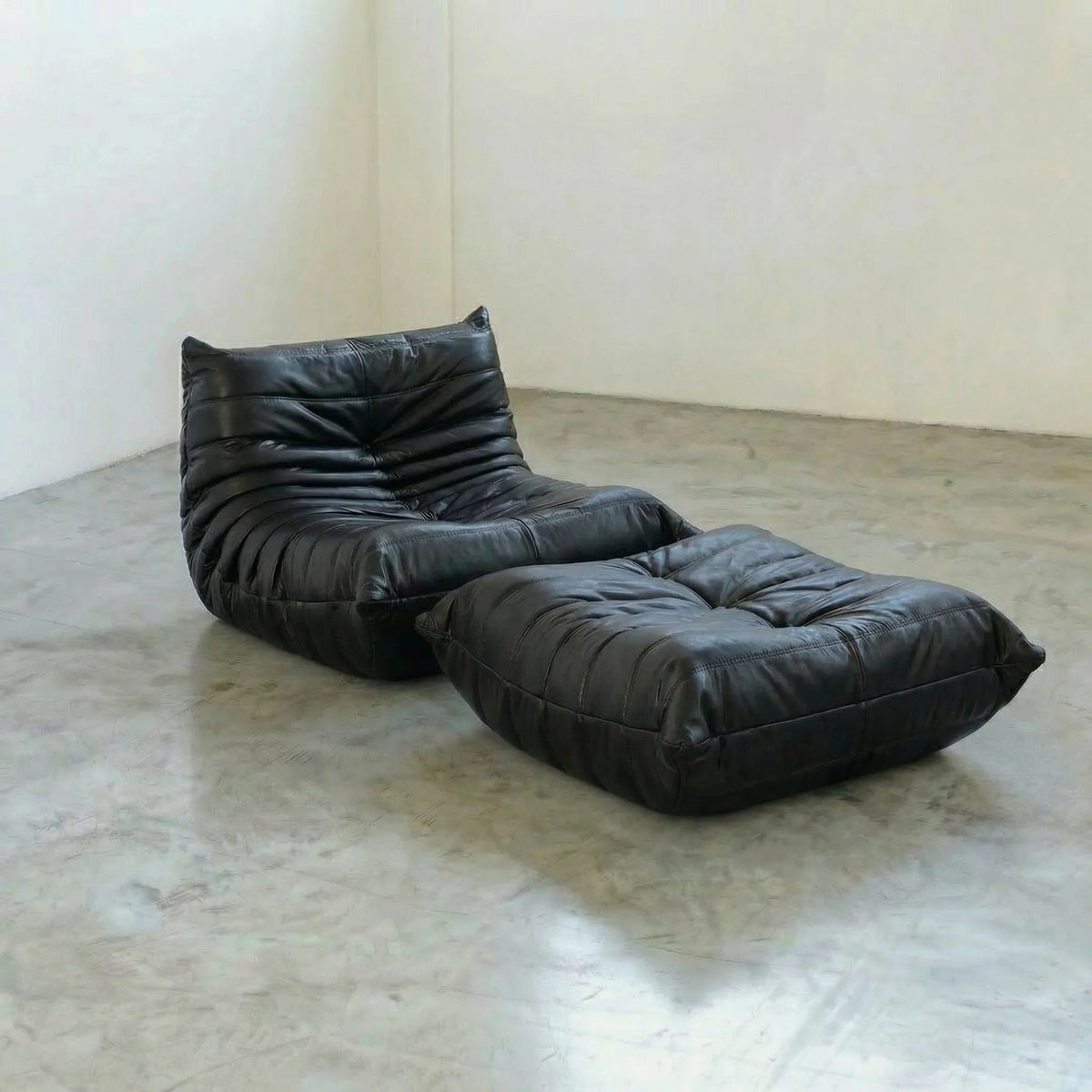 Black real leather Bruma lounge chair and ottoman on a concrete floor with white walls, by vibehaus