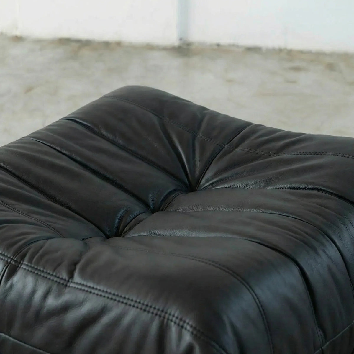 Close-up of a black Bruma leather ottoman with a blurred background